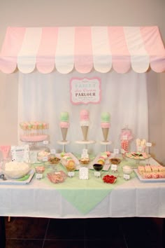 a table topped with lots of desserts under a pink and white awning