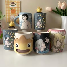 four mugs with anime characters on them sitting next to each other in front of a vase