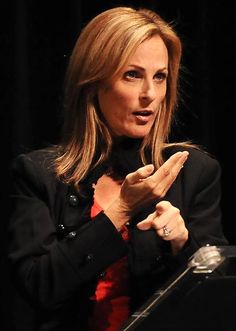 a woman standing in front of a microphone giving a speech at a podium with her hands up