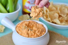 a hand holding a cracker over a bowl of dip