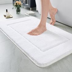 a person standing on a white rug in front of a bathtub with their bare feet sticking out