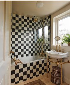 a bathroom with black and white tiles on the wall, sink and bathtub next to a window