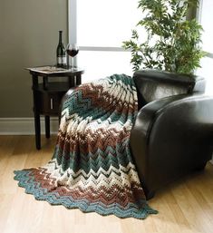 a couch with a blanket on it next to a table and a chair in front of a window