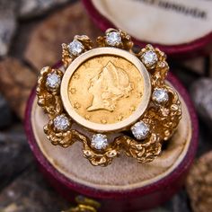 This vintage ring is centered with a replica of an 1852 $1 American gold coin set in a bezel. The coin is accented with eight round brilliant cut diamonds that are all prong set. The ring is crafted of 14k yellow gold and shows patina. It is currently a size 6.75. Vintage Jewelry With Diamond Accents For Collectible, Heirloom Coin Jewelry Collectible, Heirloom 14k Gold Coin Jewelry, Vintage Gold Jewelry With Bezel Setting, Vintage Diamond Medallion Jewelry, Antique Collectible Jewelry With Bezel Setting, Vintage Diamond Jewelry With Bezel Setting, Vintage Yellow Gold Jewelry With Bezel Setting, Vintage Round Jewelry With Bezel Setting