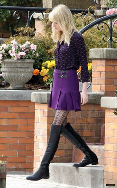 a woman in purple dress and black boots walking up steps with her hand on her hip