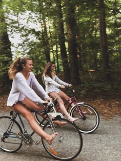 two women riding bikes down a road in the woods