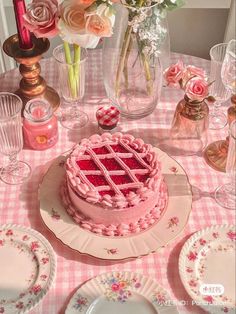 a pink cake sitting on top of a table next to plates and vases filled with flowers