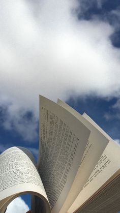 an open book sitting on top of a wooden table under a blue sky with clouds