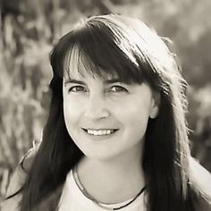 a black and white photo of a woman with long hair smiling in front of tall grass