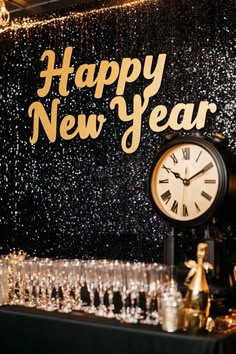 a happy new year sign with champagne glasses and a clock on a table in front of it