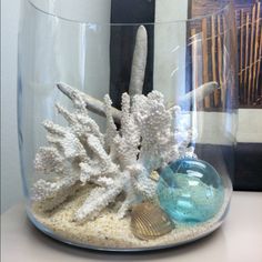 there is a glass bowl with corals and other things in it on the table