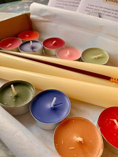 several candles are sitting in small tins on a table next to papers and pencils