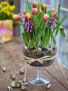 a glass vase filled with lots of flowers on top of a wooden table next to quails