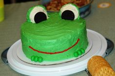 there is a green cake with a frog face on it and a cracker next to it