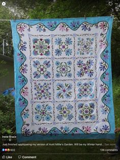 a blue and white quilt hanging on a clothes line with trees in the back ground