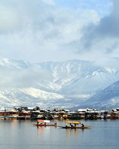 two small boats floating on top of a lake next to snow covered mountain range in the distance