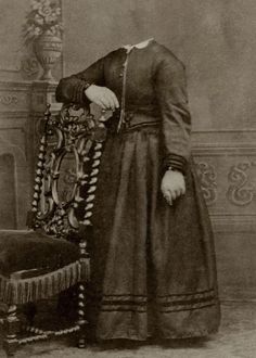 an old black and white photo of a woman in a long dress sitting on a chair