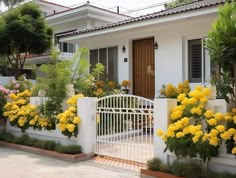 a white house with yellow flowers in the front yard and gated entry way to it