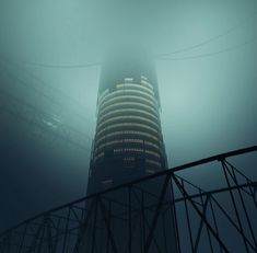 a very tall building in the fog with lights on it's side and some power lines below