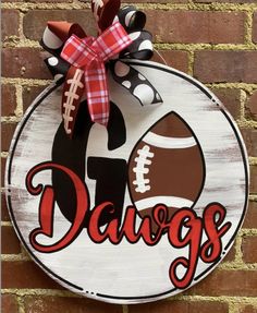 a wooden sign that says dawgs with a football on it and a bow