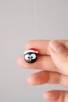 a hand holding a tiny penguin with a santa hat on it's head and nose