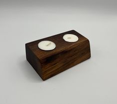 two white candles sitting on top of a wooden block with one candle in the middle