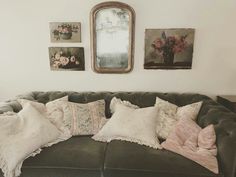 a green couch with pillows on it in front of a mirror and pictures above the couch