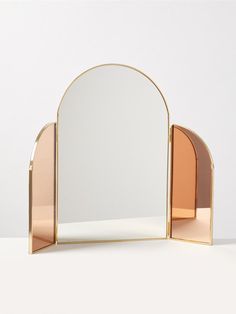 an arch shaped mirror on top of a white table next to a pink and gold shelf