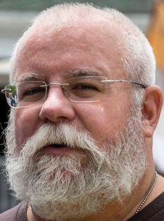 an older man with a white beard and glasses looking off to the side while standing in front of a building