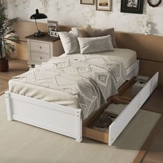 a white bed with drawers underneath it in a room next to a plant and pictures on the wall