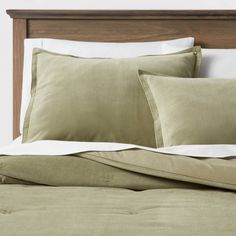 a bed with green sheets and pillows on top of it in a white walled room