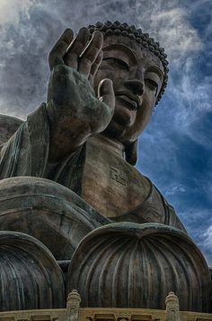 a large buddha statue sitting on top of a lush green field under a blue cloudy sky