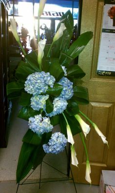 a bouquet of blue and white flowers sitting on top of a metal stand in front of a door