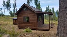 a small wooden cabin in the middle of a forest with trees and grass around it