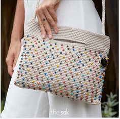 a woman is holding a crocheted purse in her hand and wearing white pants