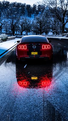 a red sports car driving down a wet road in the rain with its tail lights on