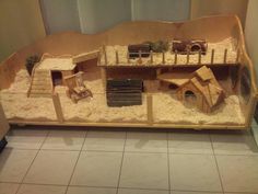 an animal house made out of cardboard and sand in a room with tile flooring