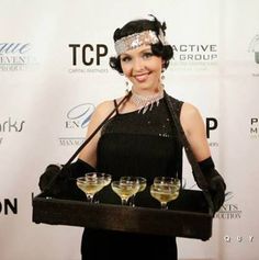 a woman in black dress holding tray with glasses on it and smiling at the camera