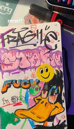 a book with graffiti written on it next to some markers and pencils in the background