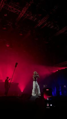 a woman standing on top of a stage in front of red and blue lights with microphones