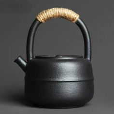 a black tea pot with a wooden handle on a gray background, the kettle has a corked top