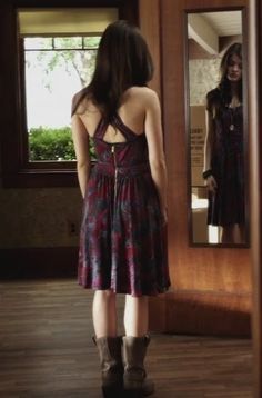 a woman standing in front of a mirror looking at her reflection wearing boots and a dress