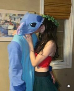 a man in a blue bear costume kissing a woman wearing a red top and green skirt