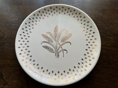 a white plate with gold designs on it sitting on top of a wooden table next to a knife and fork