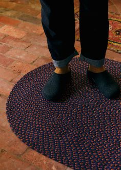 a person wearing black shoes standing on a blue and red rug in front of a brick floor