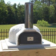 an outdoor wood burning oven on top of a wooden table in front of a fence