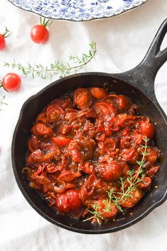 tomato sauce in a skillet with tomatoes and herbs on the table next to it