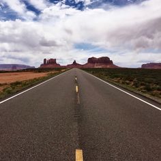 an empty road in the middle of nowhere with mountains in the background and clouds in the sky