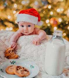 a baby wearing a santa hat sitting in front of cookies and milk