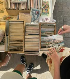 two people sitting at a table with many books and magazines on it, one person is holding an open book